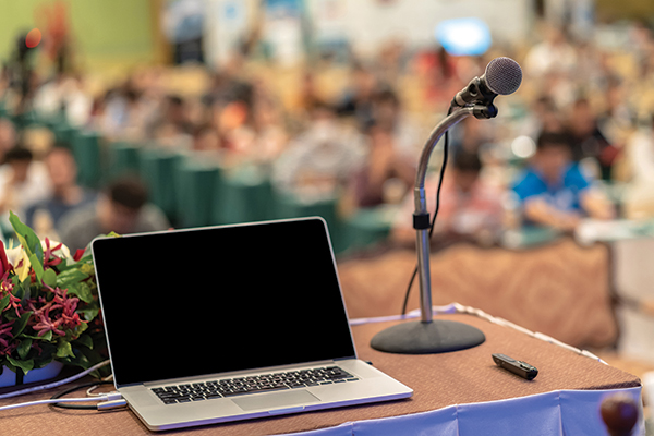 A podium with a laptop and microphone in front of a crowd.