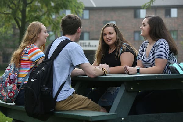 Students sitting on a picnic table in front of a residence hall