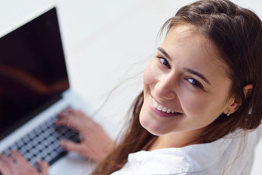 A young woman smiles up from her laptop