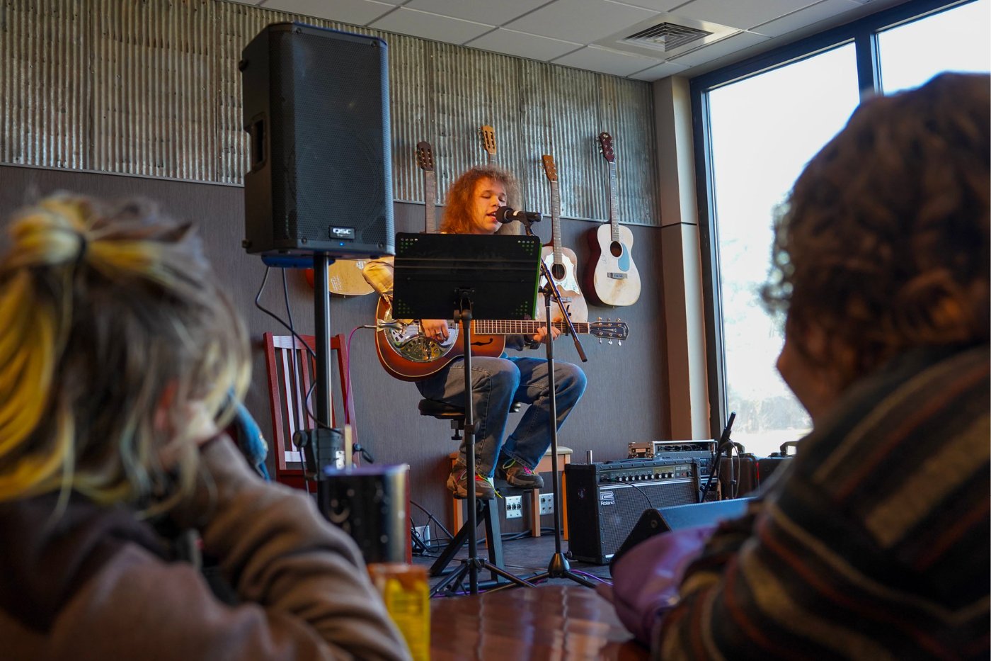 A student performs on stage in Einstein Bros. Bagels. Two students in the foreground listen.