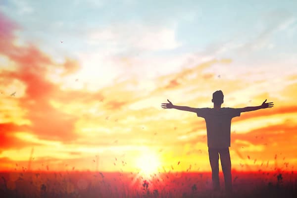 Man with outstretched arms watching the sun rise