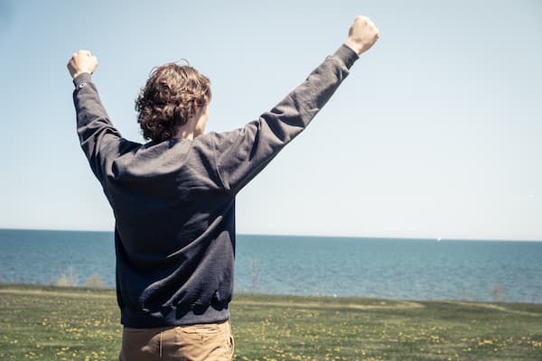 Student poses with raised arms looking over lake