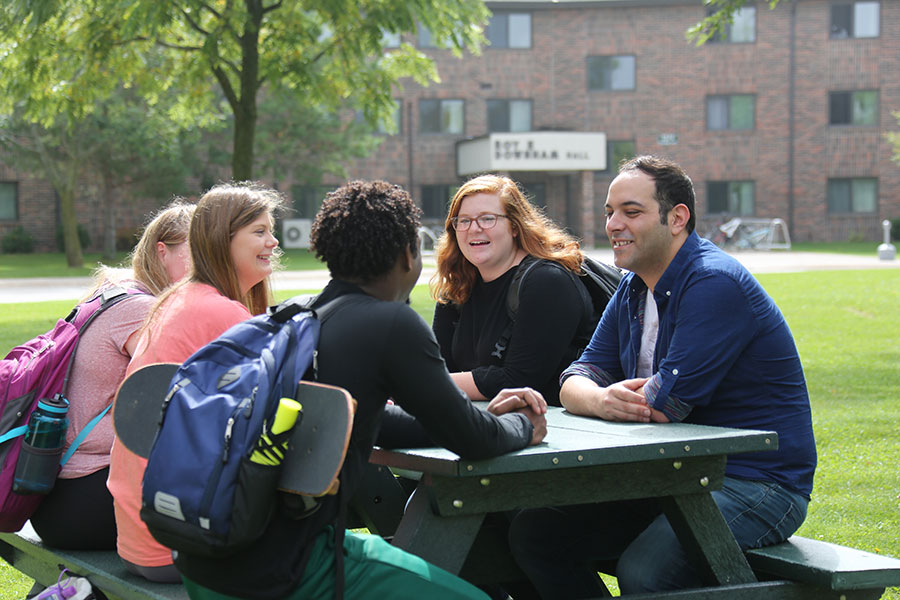 Students gathering on a picnic table by a dorm