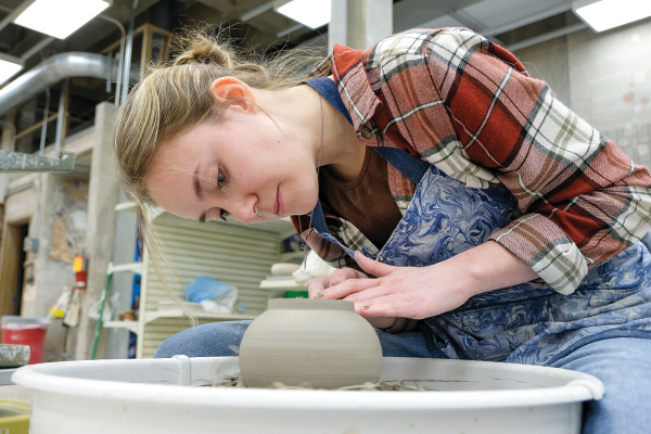 Student trimming their ceramic vessel at the potters wheel