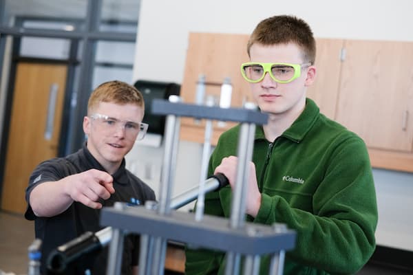 Two male students work with mechanical engineering equipment