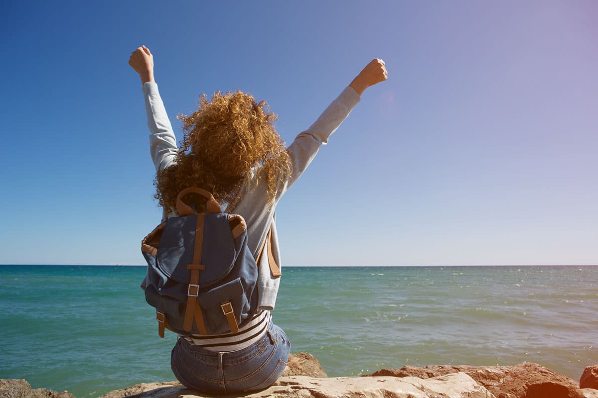 back of young woman with arms up facing lake