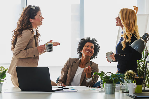 three women in an office working together holding coffee cups