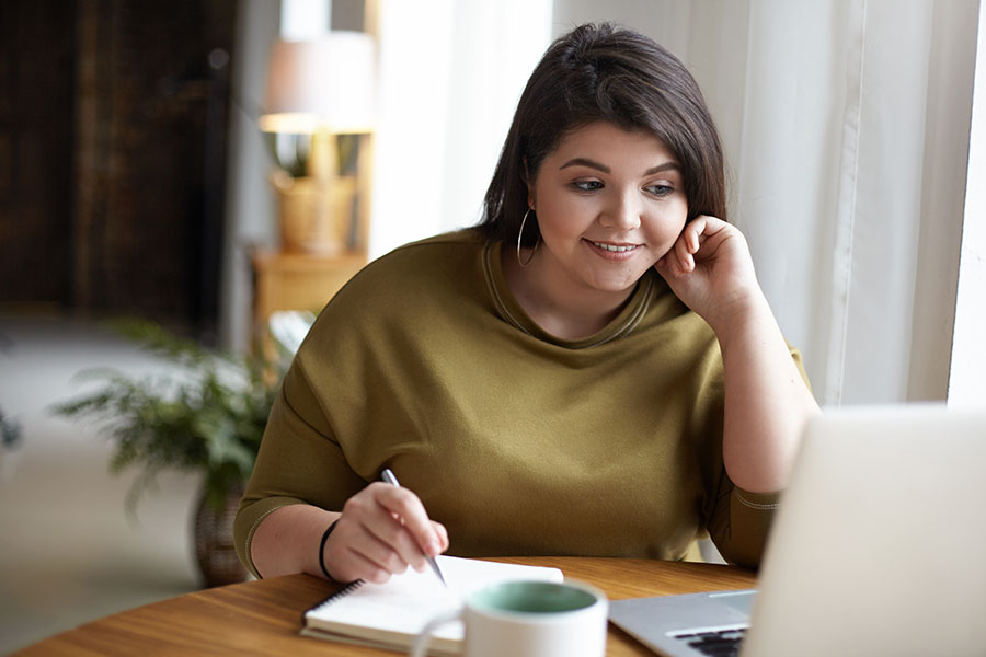 woman taking notes while watching online course