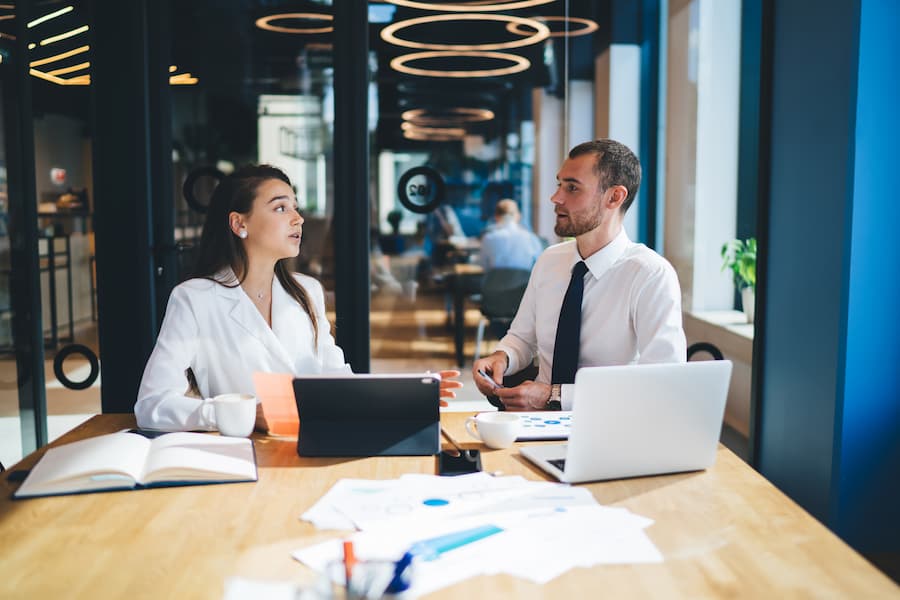 Two business employees with laptops discussing analytics