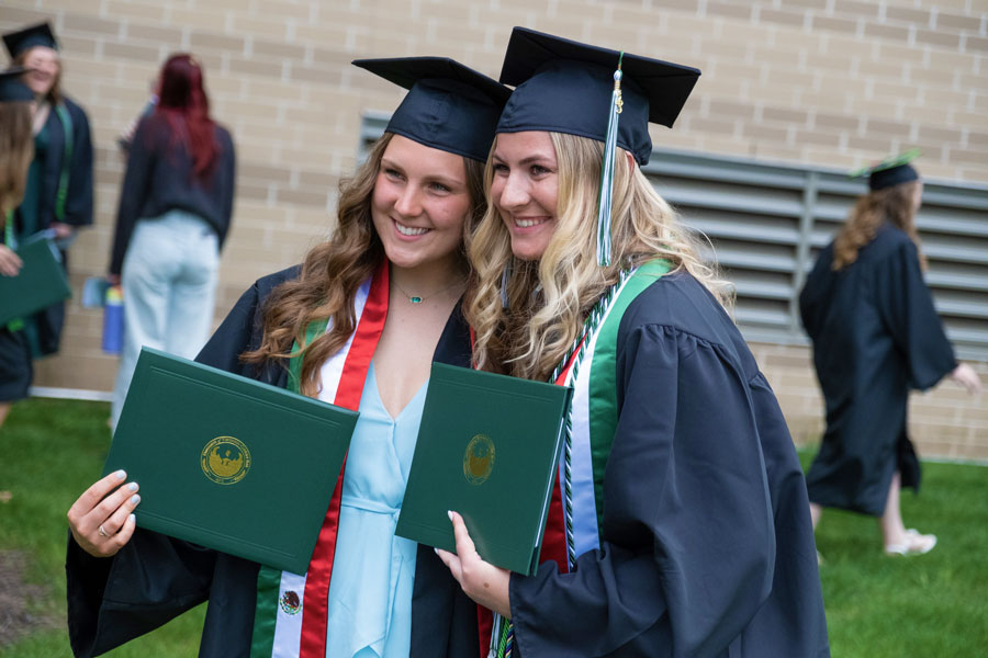 Two students posing with diplomas in cap and gown
