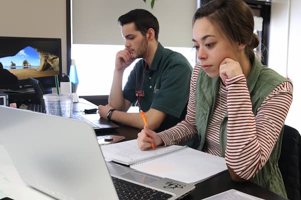 A male and female student work at lap tops in the writing center