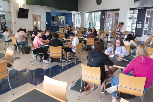 Several students sit at tables in a lounge area