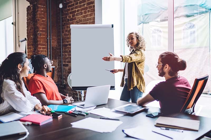 woman standing by a large notepad leading a group conversation