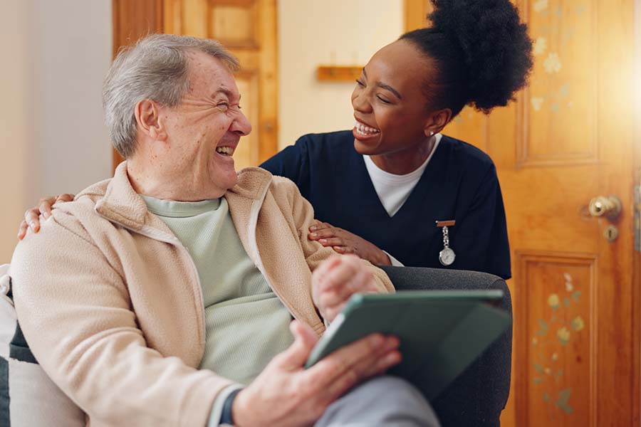 woman caregiver smiling with senior man holding tablet