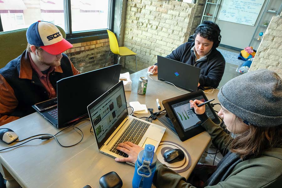 Three young men working on laptops and tablets around a table