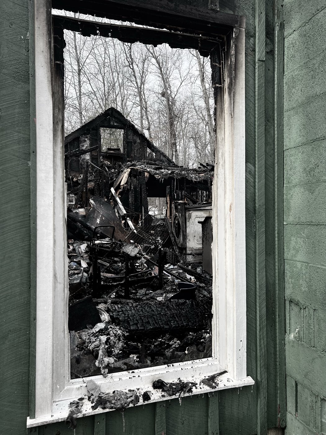 Photo: Looking through a window frame at a burned house.