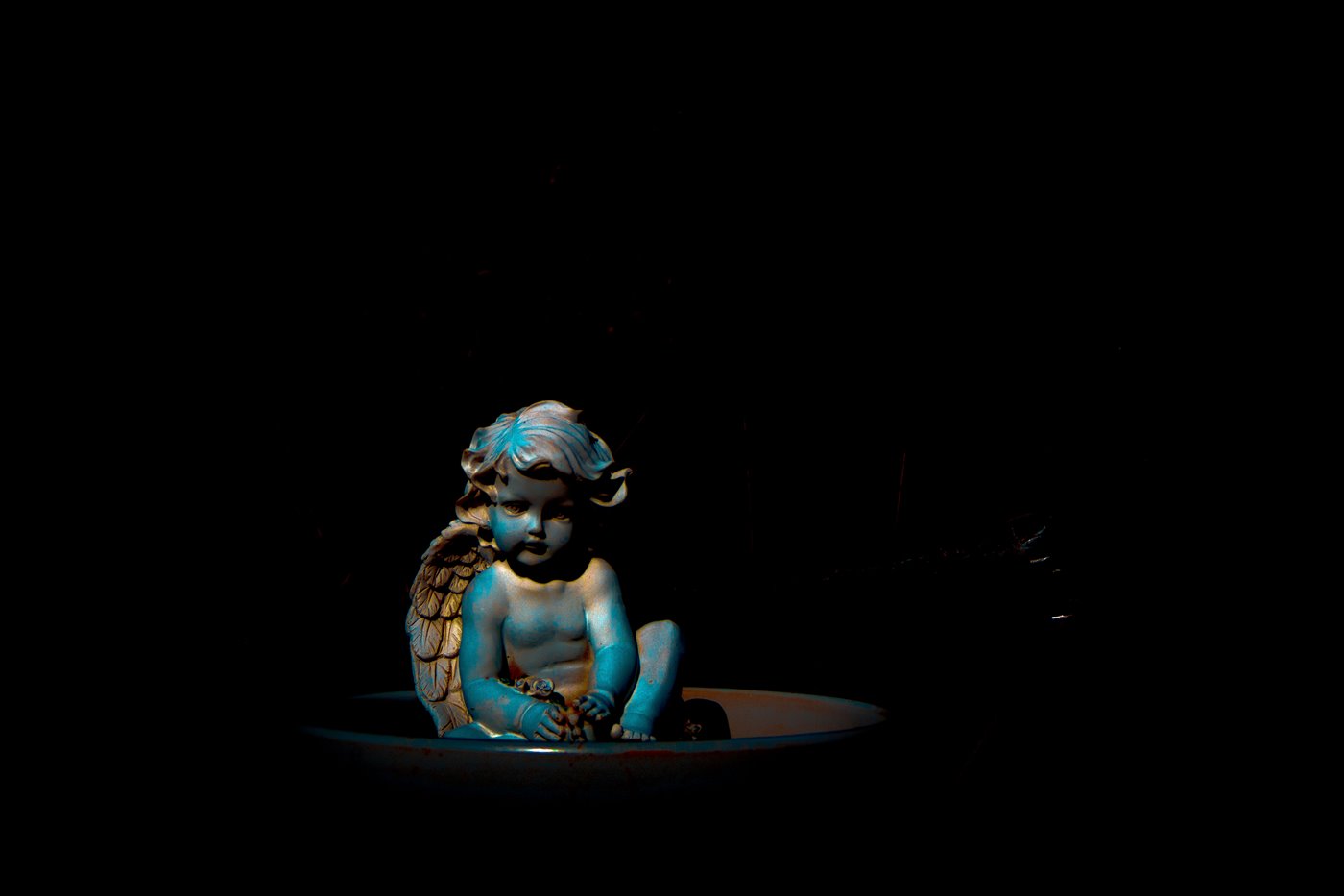 Photo: Blue cherub in a birdbath against a black background