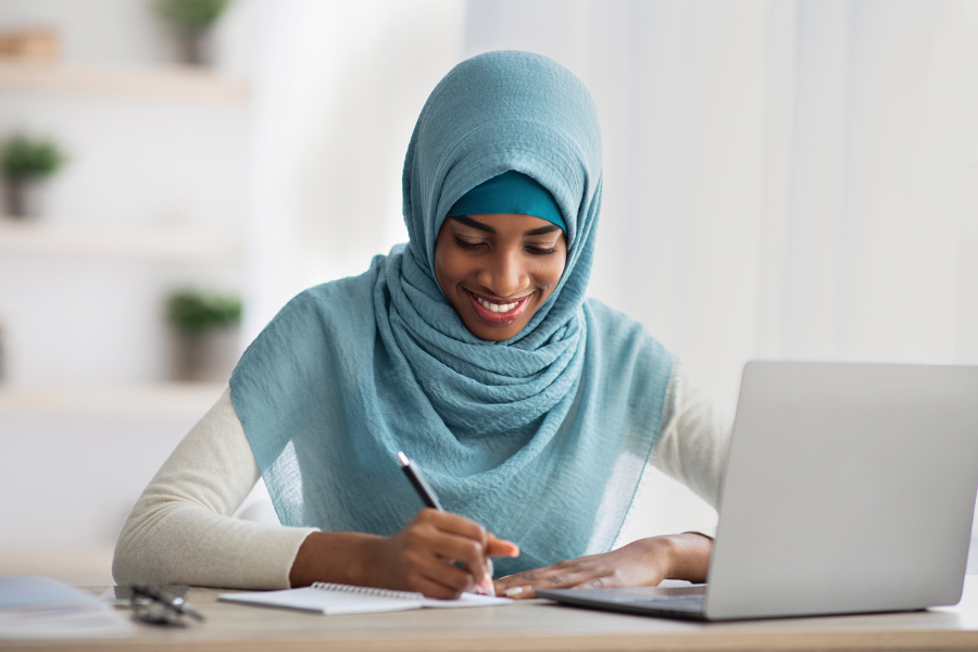 A young woman writing down notes while using her laptop