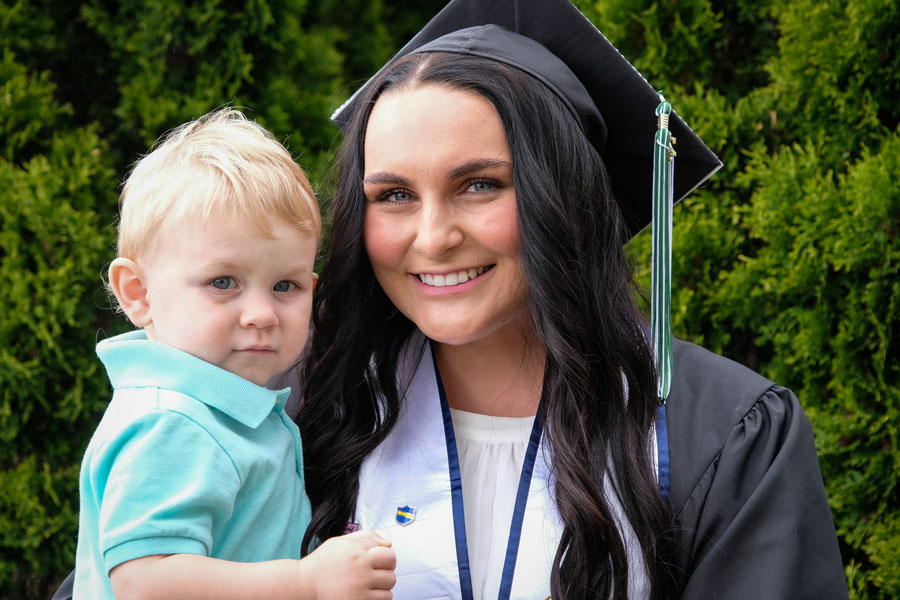 UW-Green Bay student in cap and gown holding her child