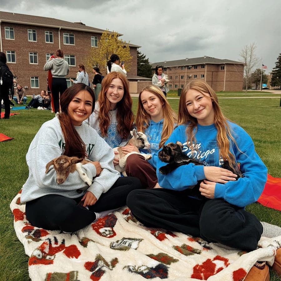 Four students sit on the lawn near UWGB dorms holding baby goats