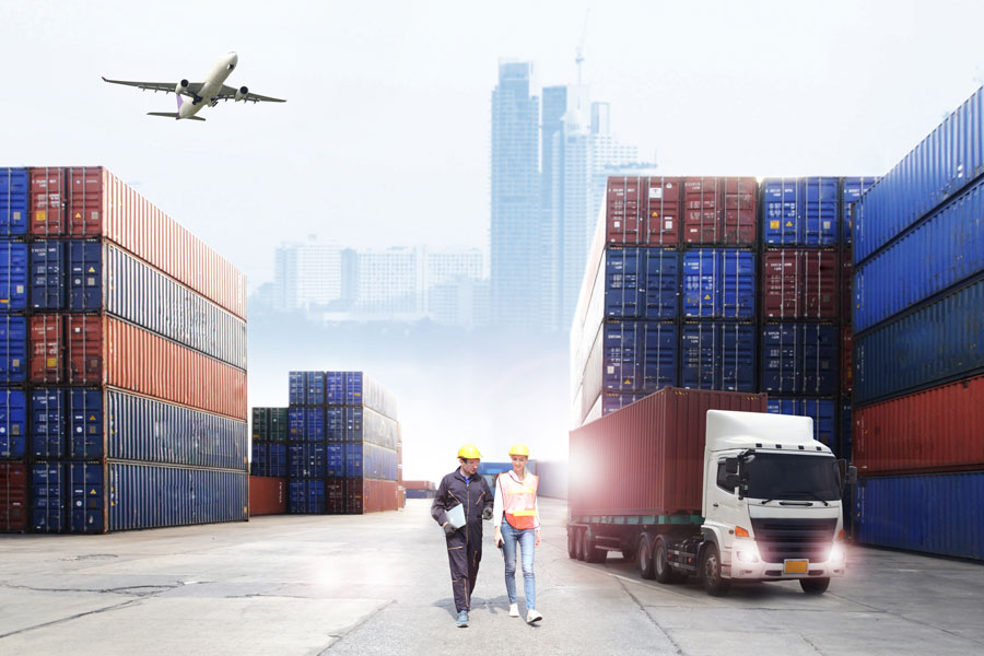 Workers in hard hats walking with shipping containers, trucks and planes in background