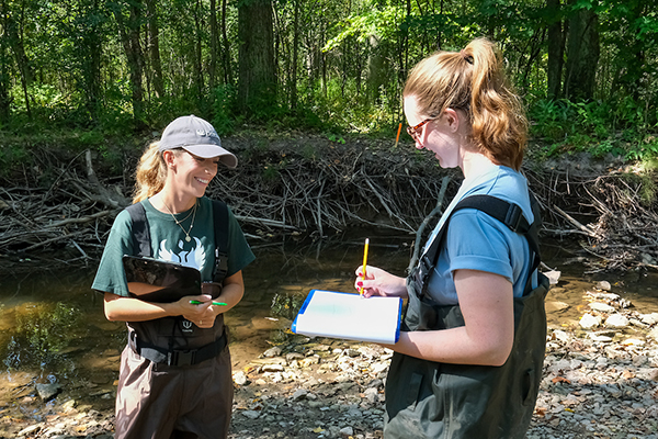 Two students recording data near stream