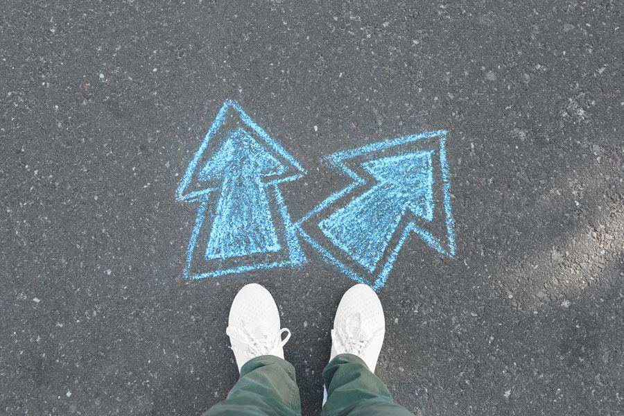 Person standing on pavement with chalk drawing of arrows