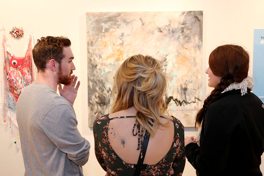 three people discussing painting in a gallery