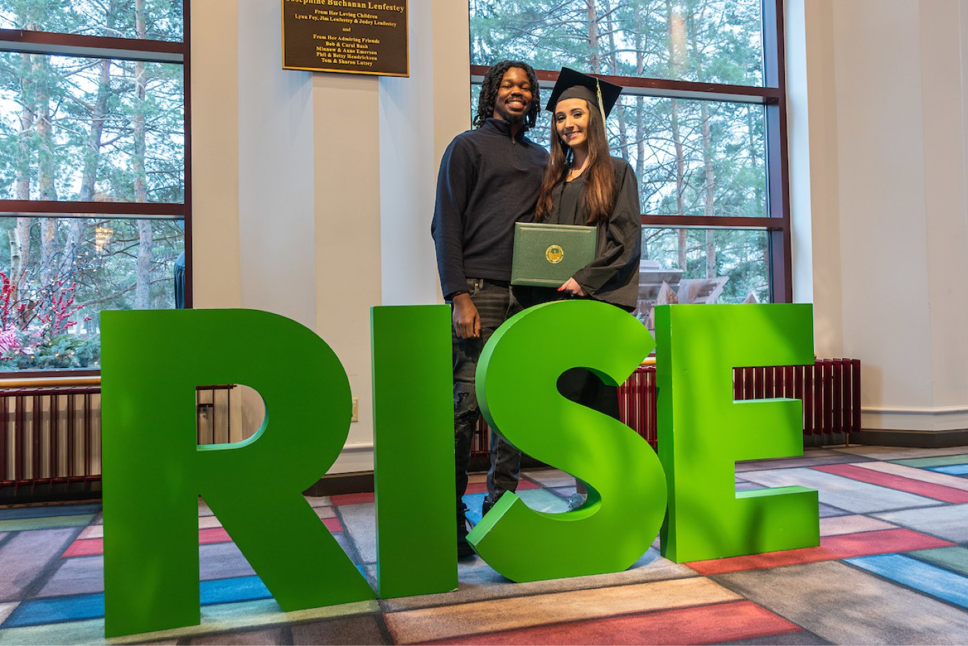 student standing by RISE letter after commencement
