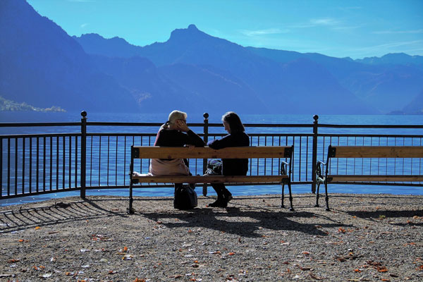 Two people sitting on bench by mountains