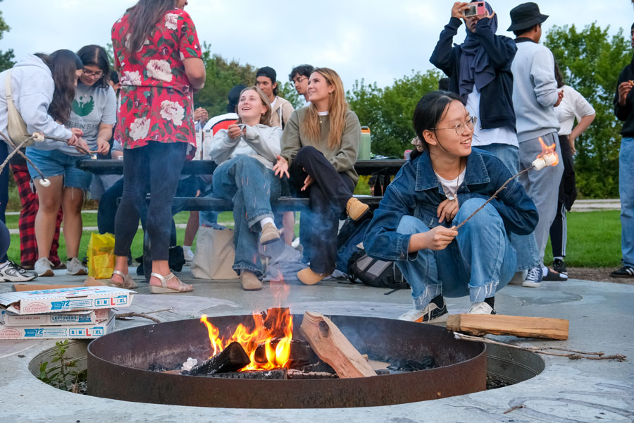 Students cooking marshmallows over fire pit