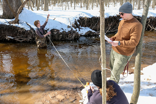 Three students collecting data in snowy stream