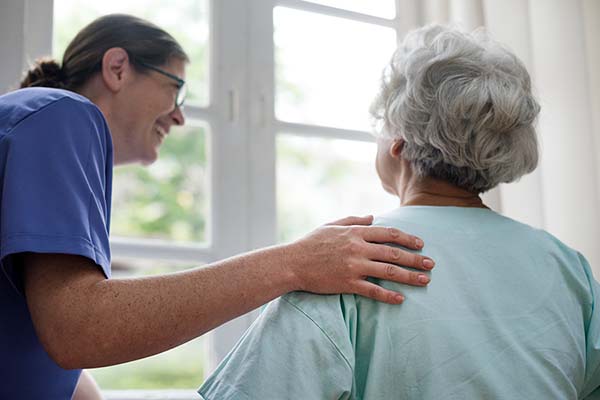 caregiver gently placing hand on elderly womans shoulder