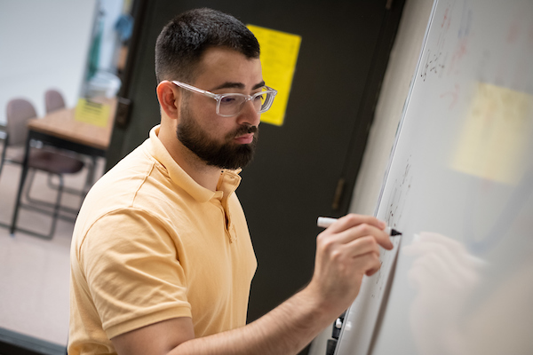 Student writes on a white board in a study room