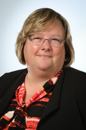 smiling person wearing glasses, a striped blouse, and a black blazer