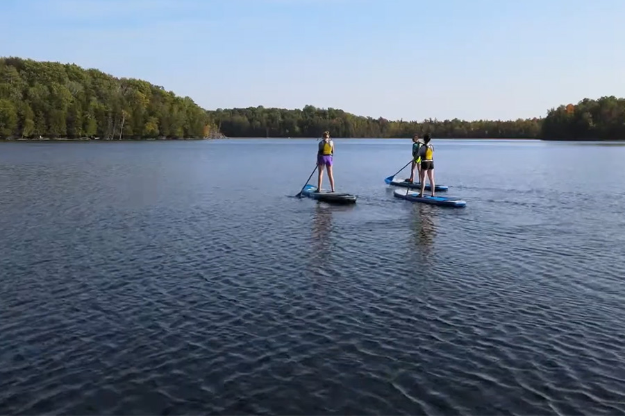 Students stand-up paddelboarding on a still body of water